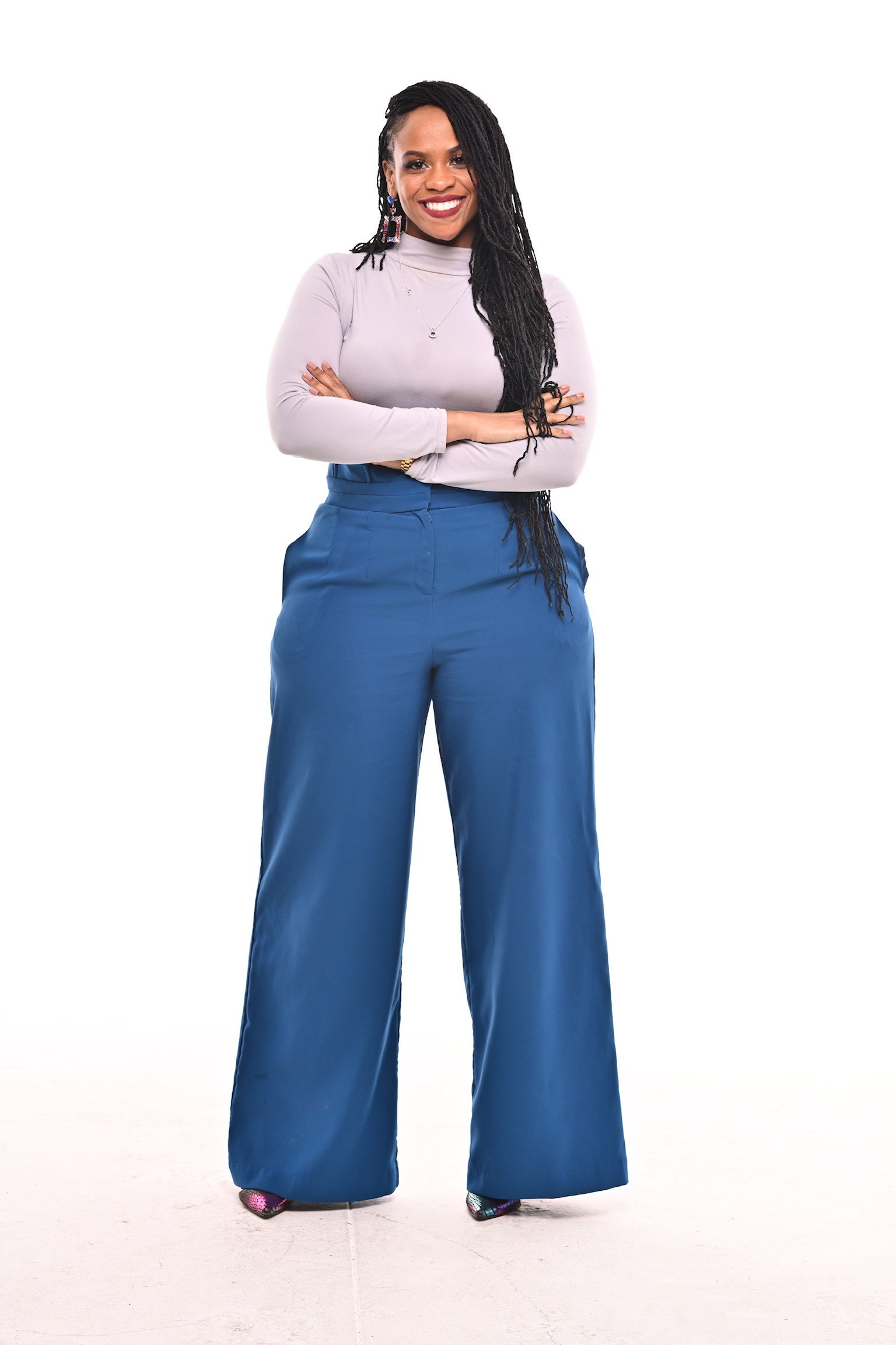 Akilah smiling with her arms folded, wearing blue trousers